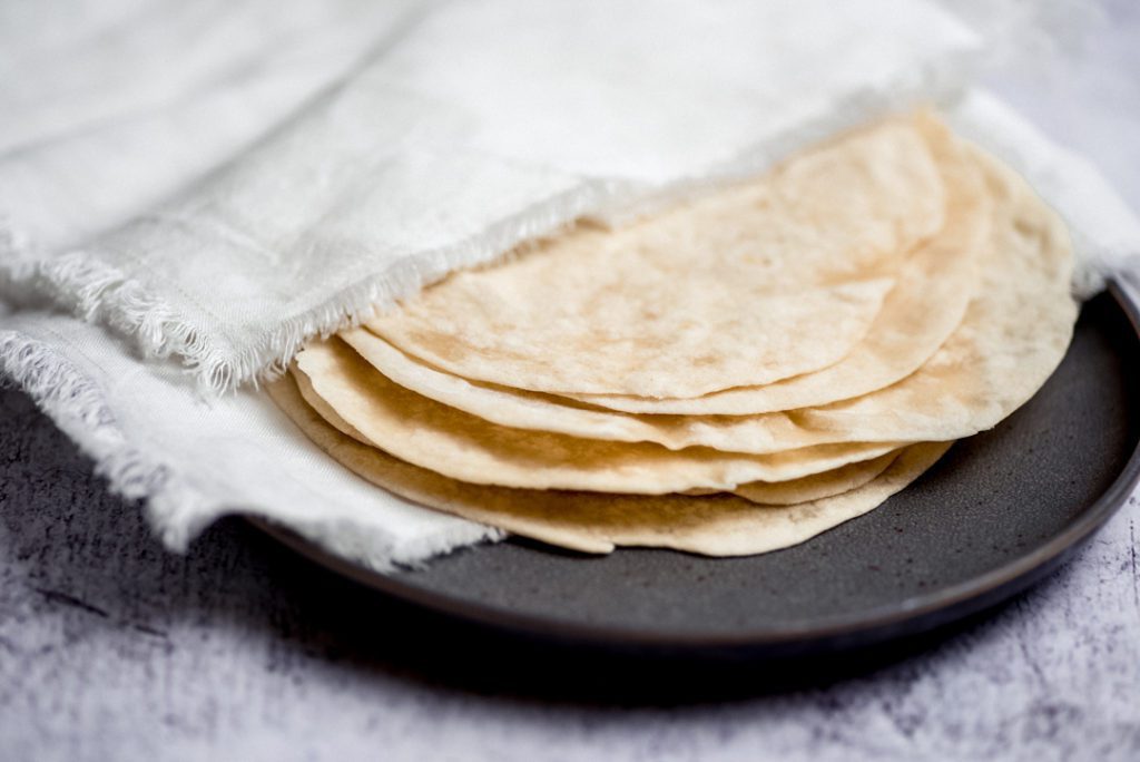 homemade flour tortillas on a plate covered by a napkin
