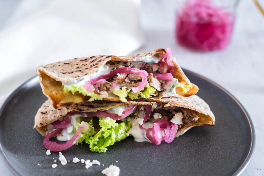 pita wrap on a plate with onion, lettuce, cheese and tzatziki sauce