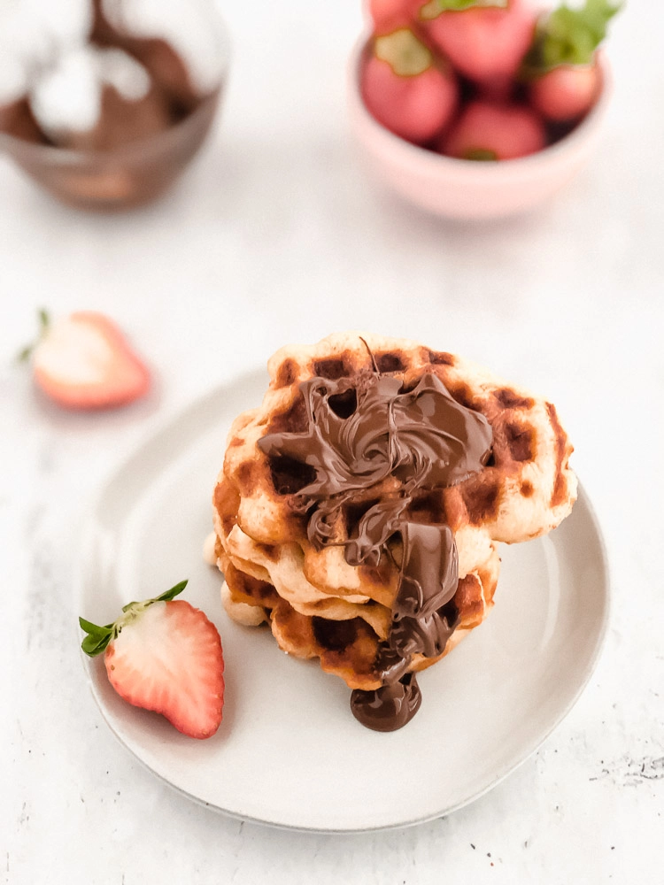 Liege waffles on plate drizzled with Nutella and strawberries