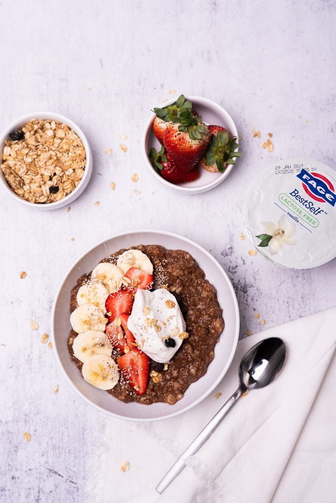chocolate protein oatmeal in a bowl with banana, strawberries and granola