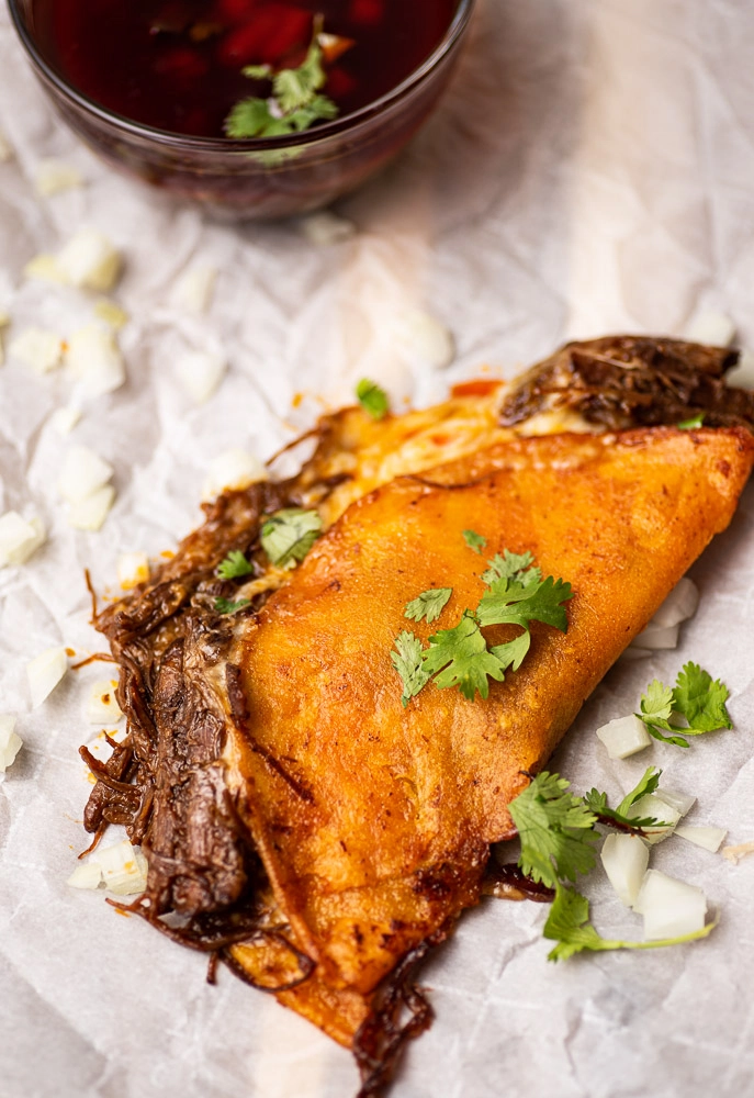 birria quesadilla served on parchment paper. garnished with onion and cilantro