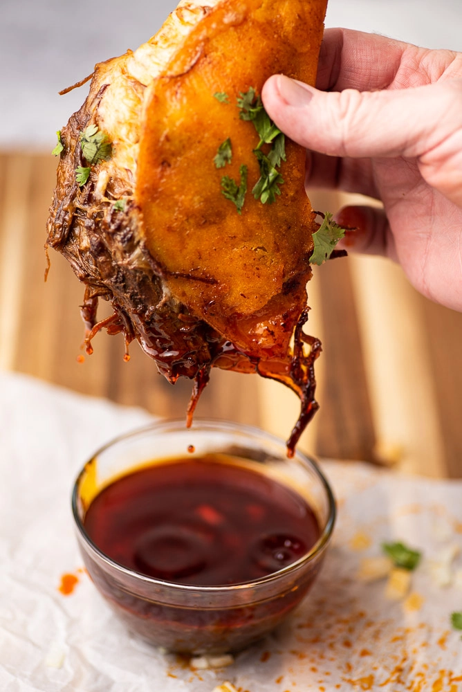 hand holding corn tortilla stuffed with cheese with dipping au jus. garnished with cilantro