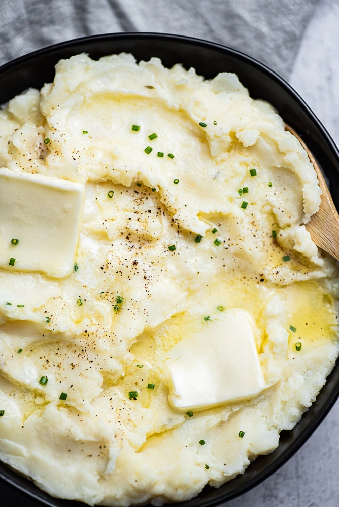Mashed potatoes in bowl with butter garnished with chives and wooden spoon