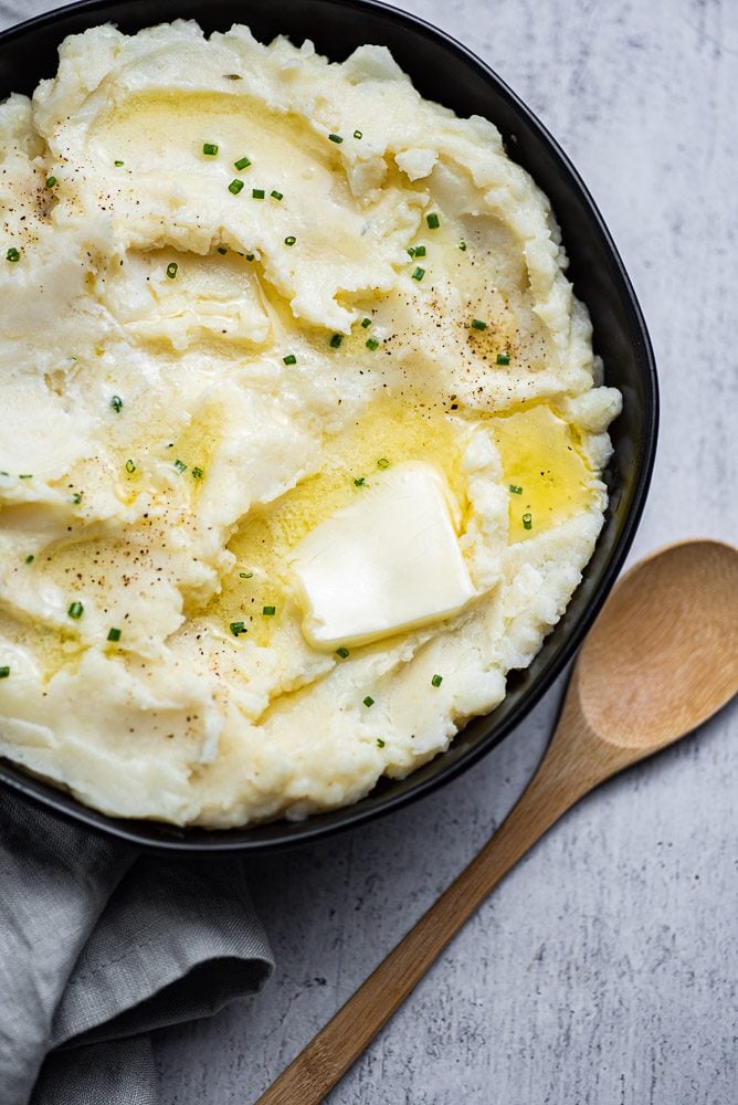 Mashed potatoes in bowl with butter garnished with chives and wooden spoon
