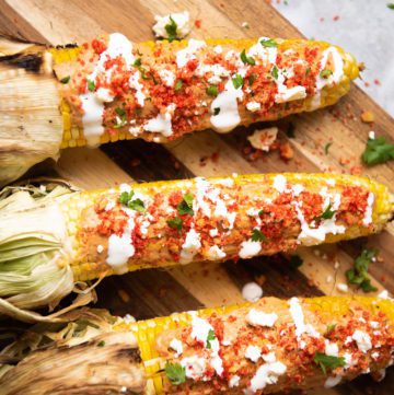 Corn on the cob with cheese, cilantro, Crema and Cheetos on a wooden board