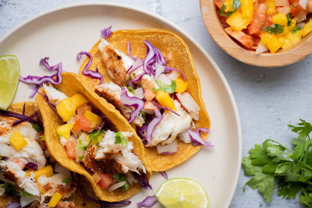 Fish tacos on a plate, cilantro and mango salsa in bowl