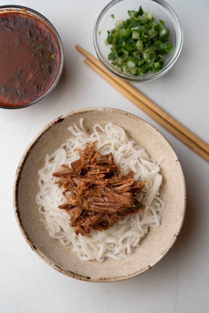 ramen with birria in a bowl. Consome in a bowl, chopped onions and cilantro in a bowl and chopsticks