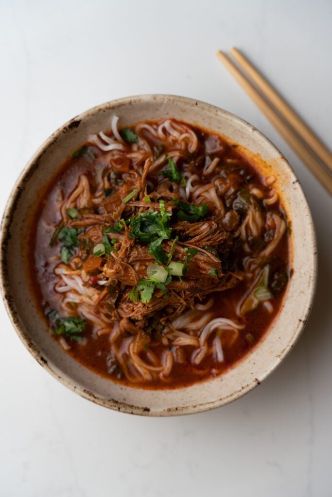 Birria ramen on a bowl garnished with cilantro and onion. Chopsticks on the side