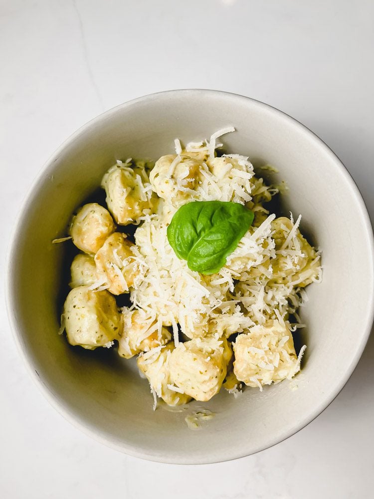 cauliflower gnocchi on a bowl with pesto creamy sauce and parmesan cheese with basil leaf