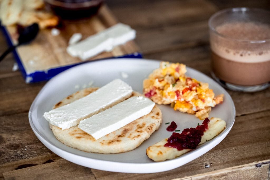 Colombian arepa topped with quesito. Eggs with tomato and scallions, hot chocolate