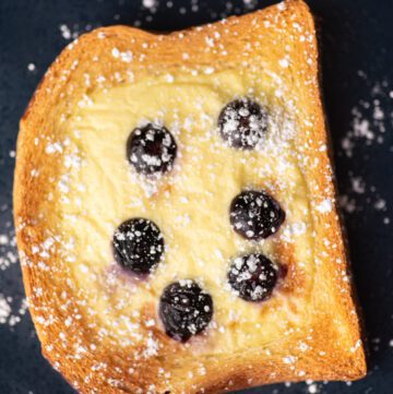Custard toast on a blue plate with blueberries and powdered sugar