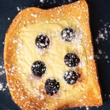 Custard toast on a blue plate with blueberries and powdered sugar