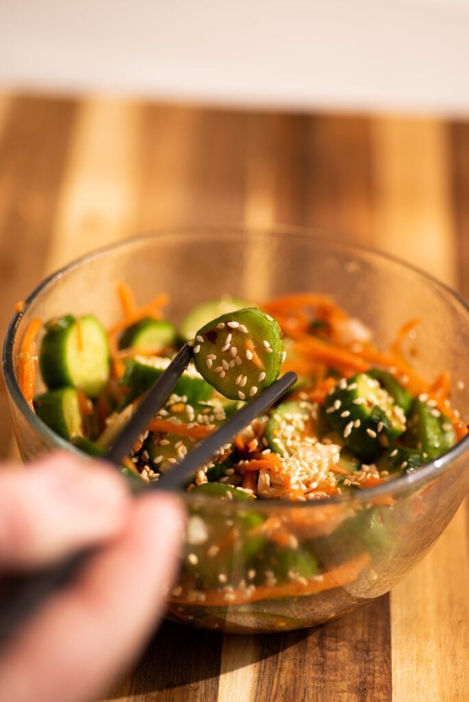 Cucumbers, carrots, sesame seeds and onion in a bowl with chopsticks
