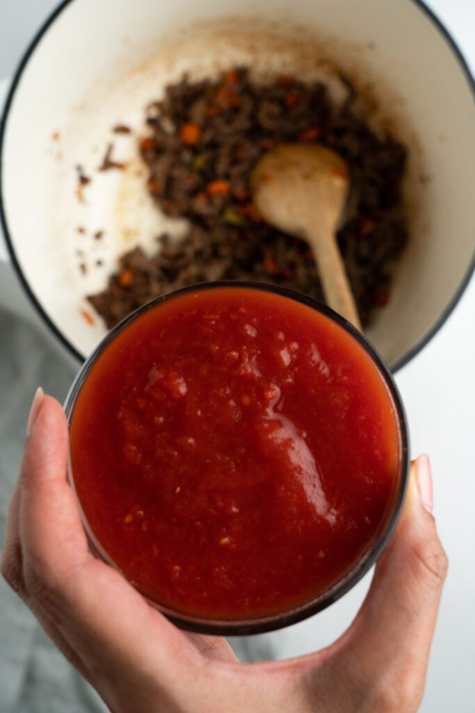 meat on pot with wooden spoon below tomato sauce on a cup