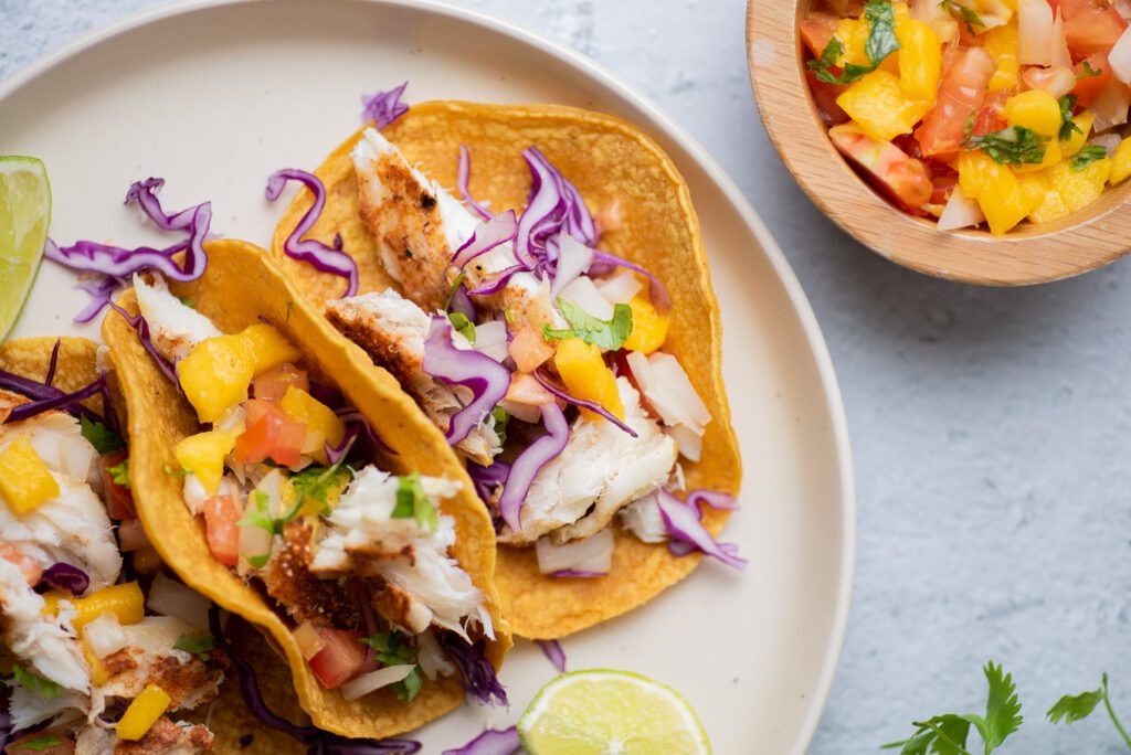 fish tacos on a plate with mango slaw on a bowl