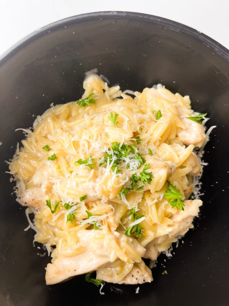 cajun chicken orzo on a black bowl garnish with parsley