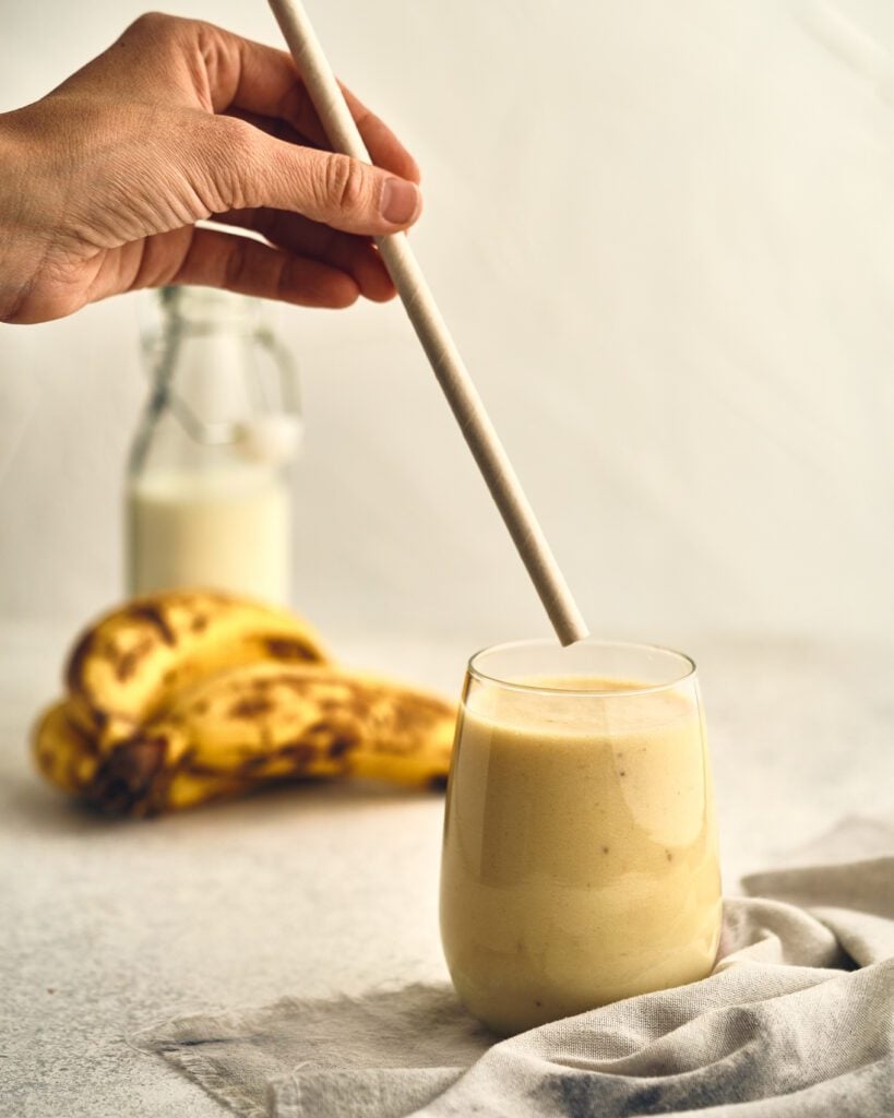 banana milk on a glass with straw and  bananas in the background