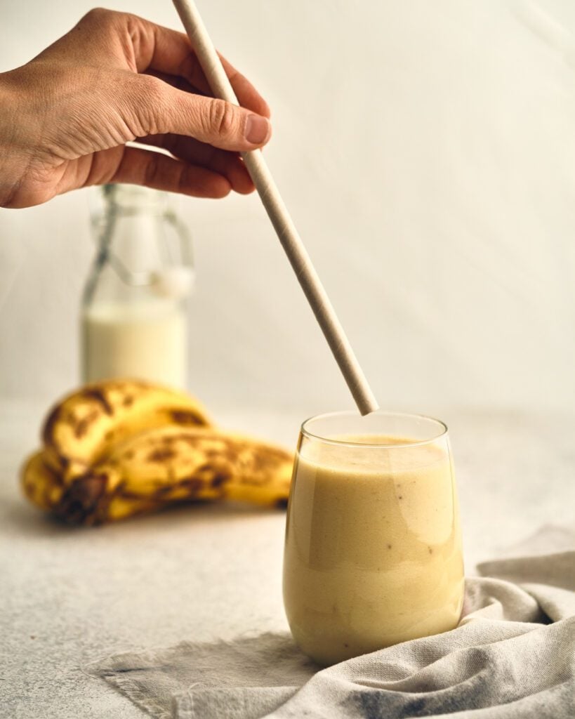 banana milk on a glass with straw and bananas in the background