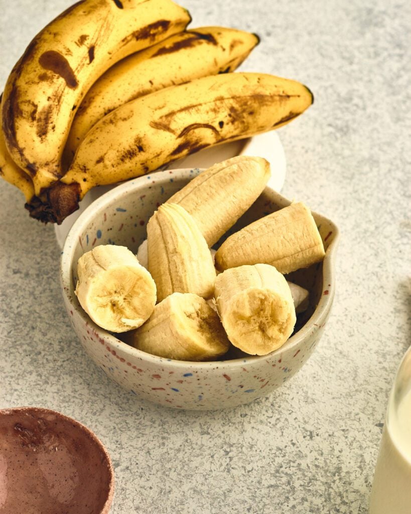 bananas in the background with peeled bananas in a bowl