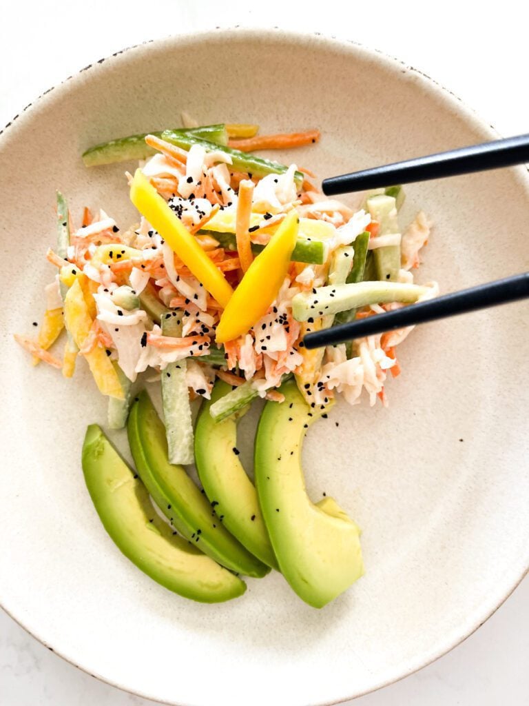 crab, cucumber, avocado and mango salad on a plate with chopsticks 