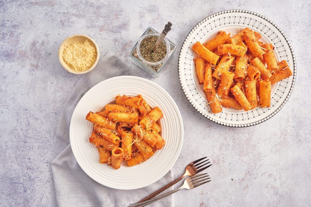 overhead of pasta plates with cheese and oregano. forks on napkin