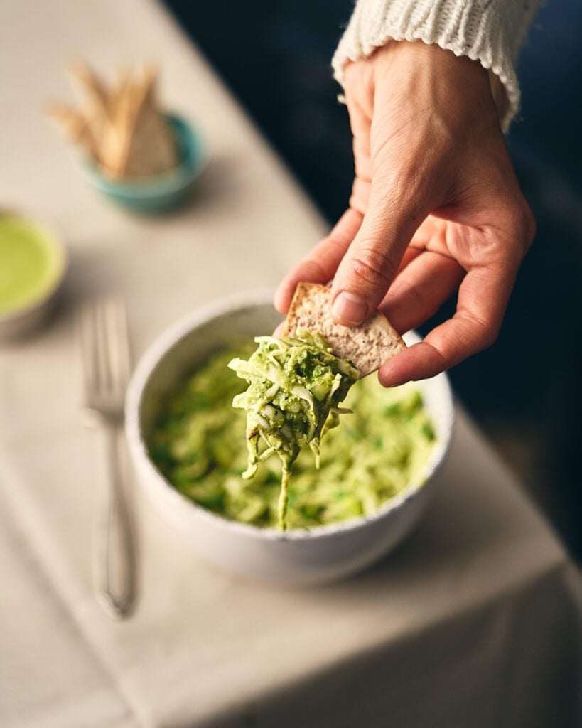 salad on a bowl being scooped with pita bread, fork on the side and pita chips in a bowl