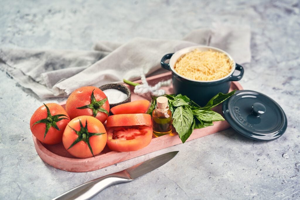 ingredients for roasted tomatoes on a board including olive oil and parmesan cheese