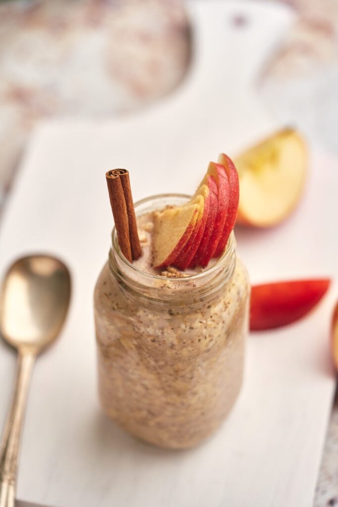 Oats in jar with apple slices and cinnamon stick with spoon