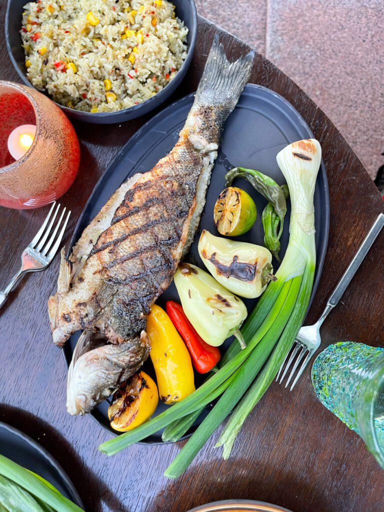 Grilled fish on a plate with veggies and rice on the side on a bowl