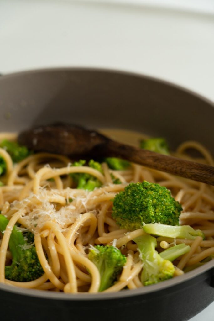 overhead view of broccoli with spaghetti in a skillet with wooden spoon