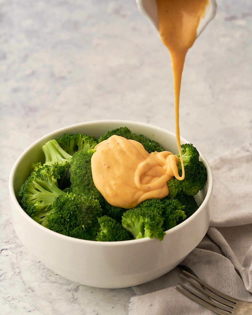 broccoli in a bowl with cheese sauce being poured over