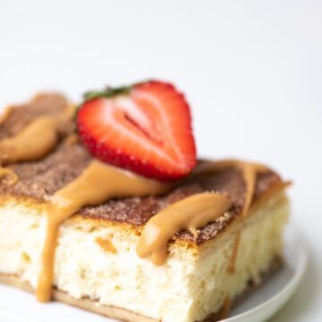 Churro cheesecake bar on a plate with caramel sauce and strawberries.