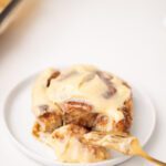 Cinnamon roll with icing on plate with fork.