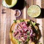 Tuna tostada with avocado and lime on a wood board.