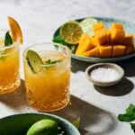 mango margarita on the rock with plate with cut up mango and pinch bowl with salt