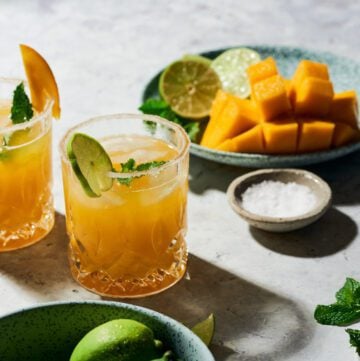 Mango margarita on the rock with plate with cut up mango and pinch bowl with salt.