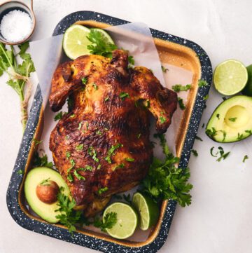 Pollo asado on a tray with lime wedges and avocado