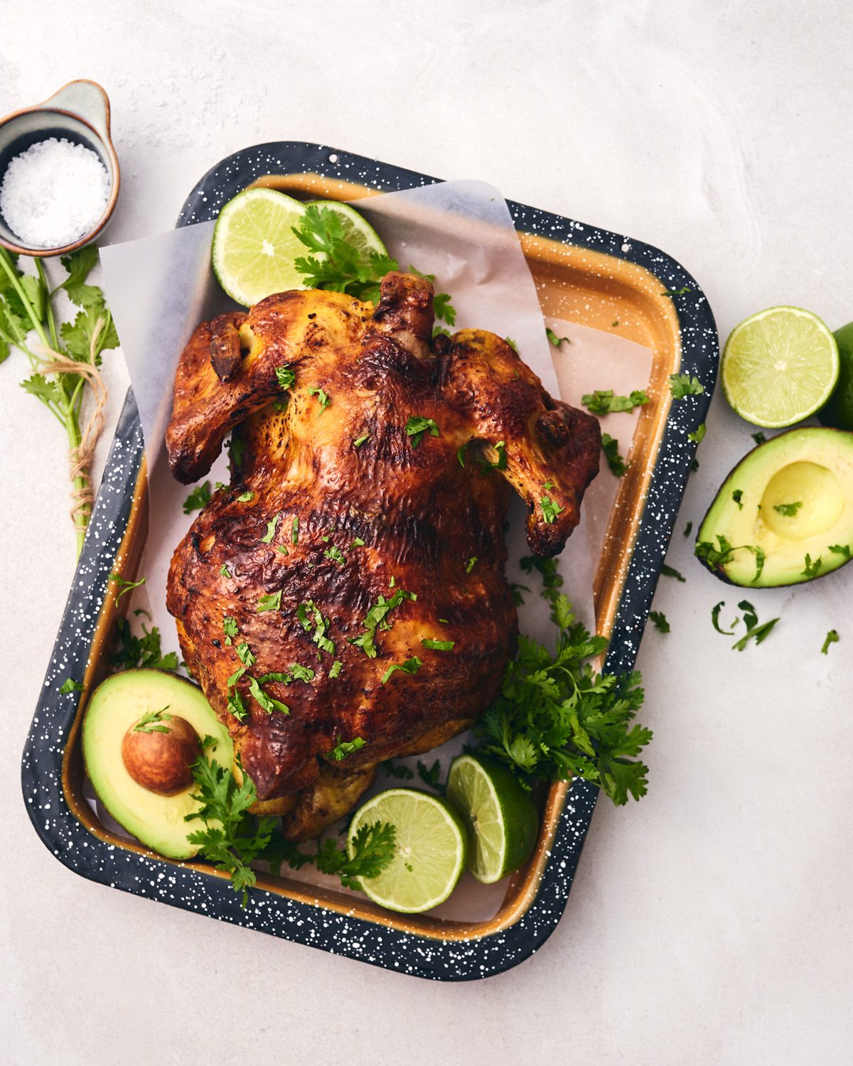 Pollo asado on a tray with lime wedges and avocado