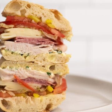 Sandwich stacked on a plate with cold cuts of meat and cheese.