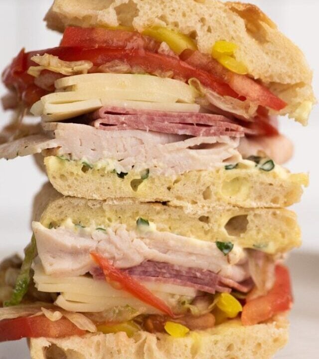 Sandwich stacked on a plate with cold cuts of meat and cheese.