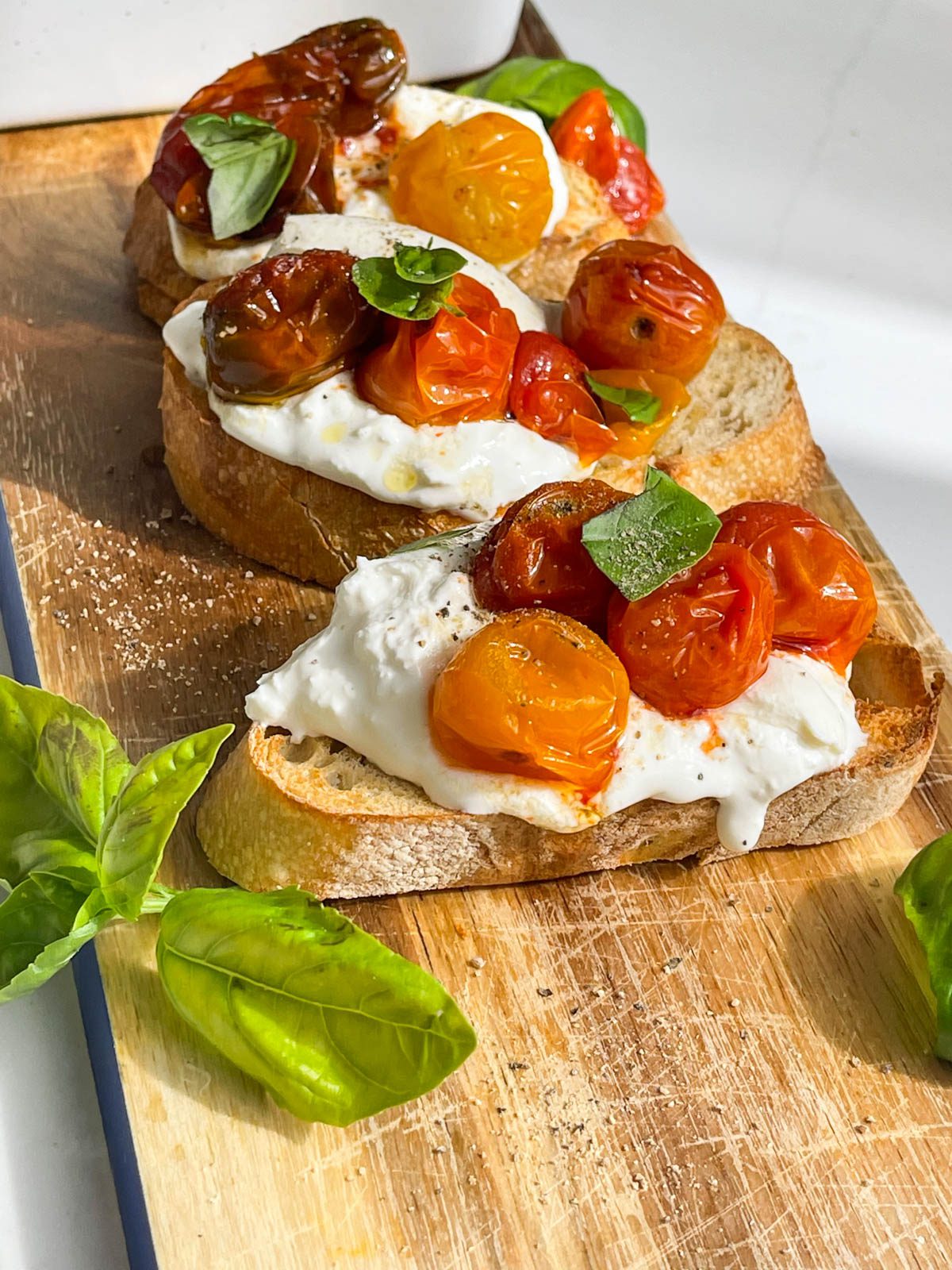 jammy tomatoes with burrata cheese on toasted bread and basil garnish on a wooden board