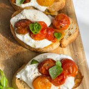 Burrata cheese on toast with tomatoes and basil on a wooden board.