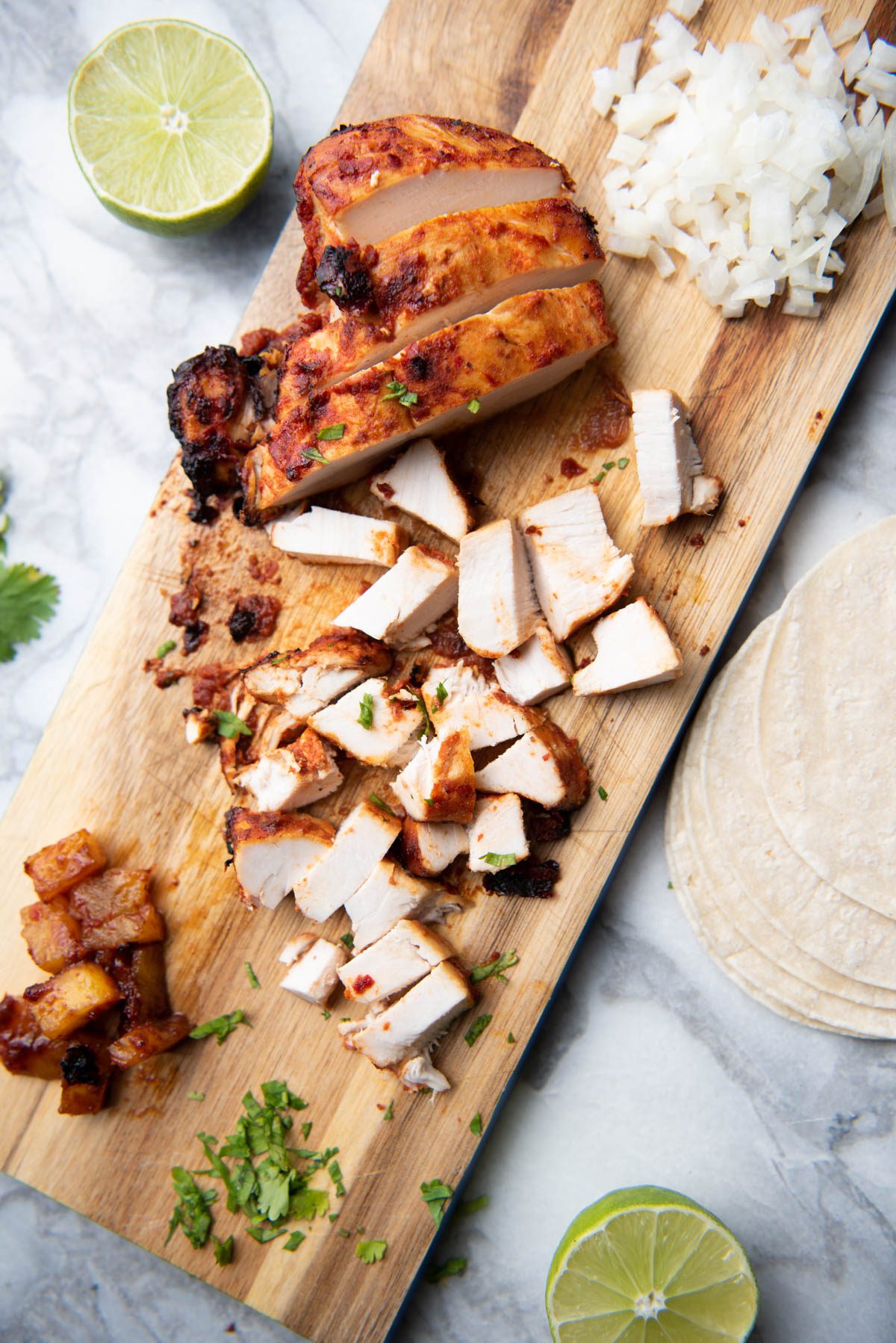 Chicken on wooden board with cilantro, pineapple and limes.