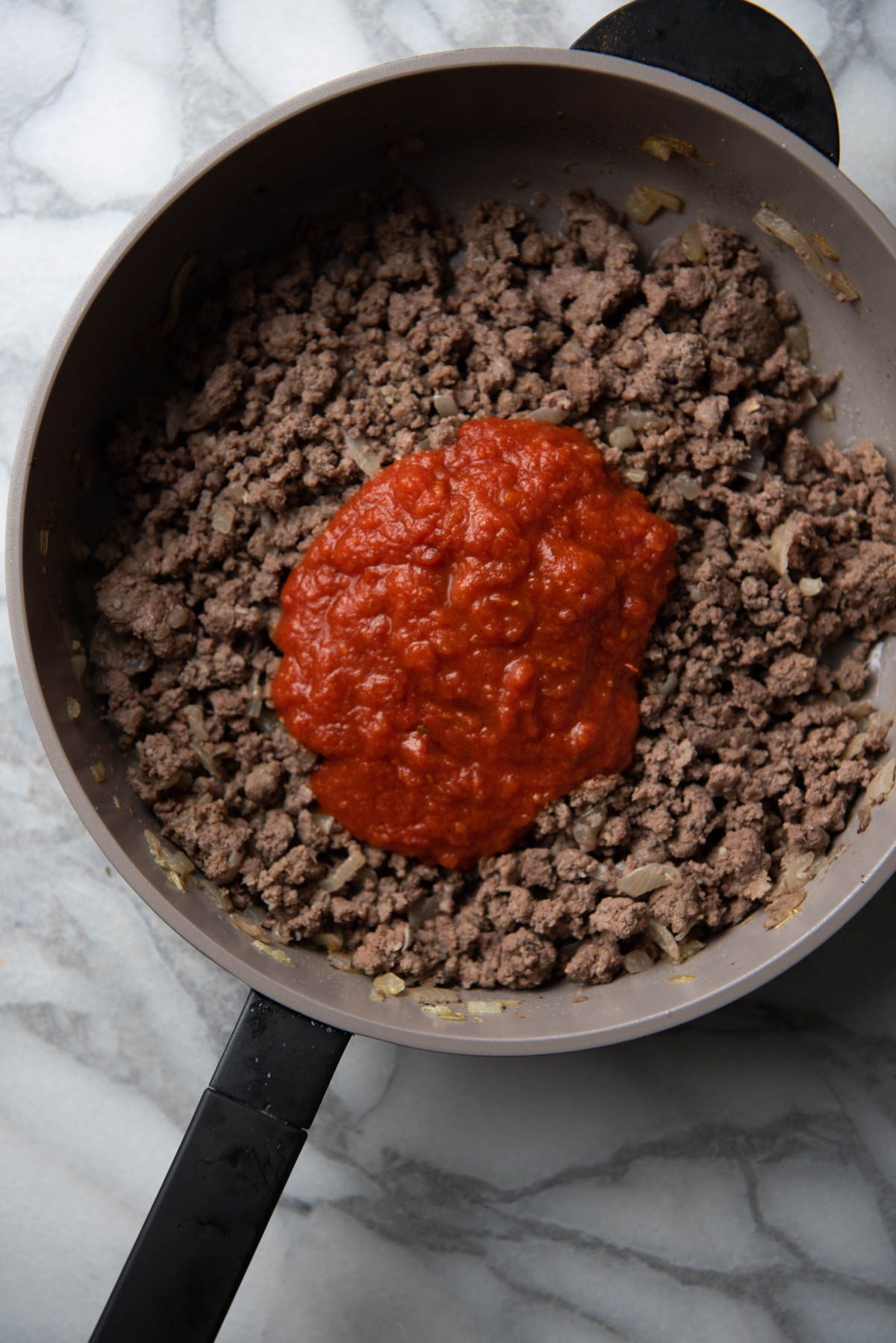 browned ground beef on a skillet with onions and marinara sauce.