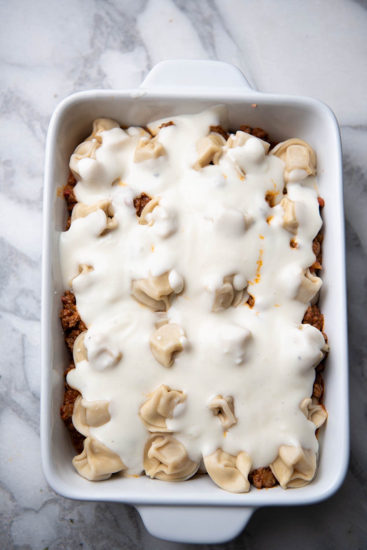 tortellini in a baking dish with marinara sauce and meat and Alfredo sauce.