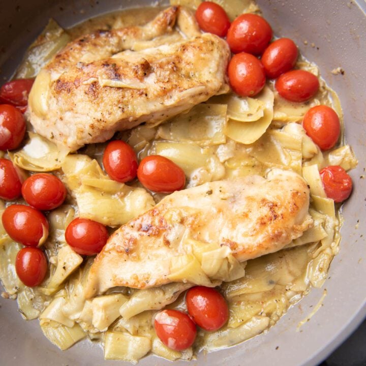 chicken with artichokes and tomatoes on a skillet.