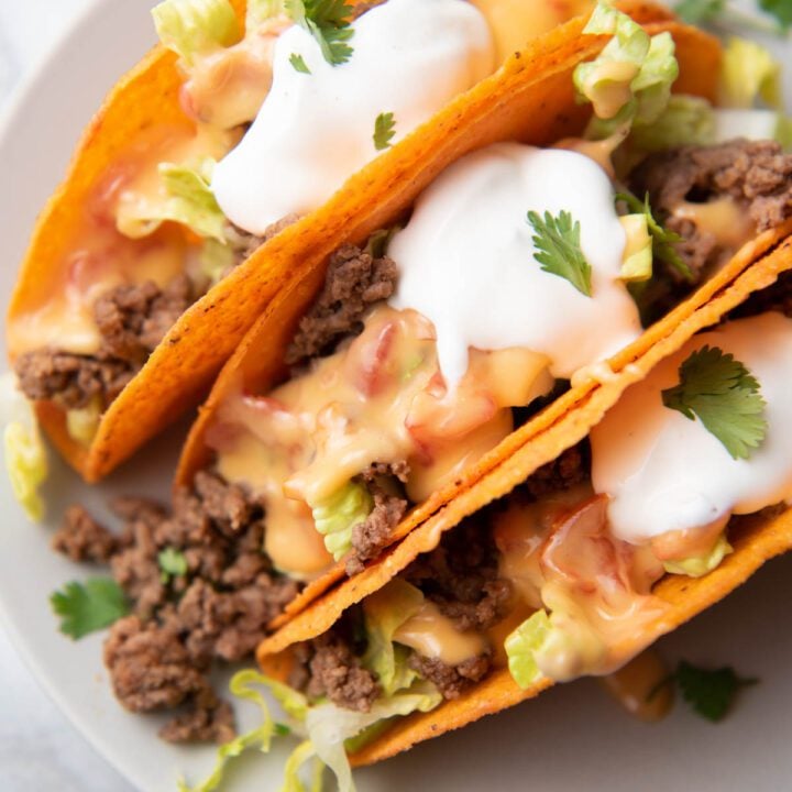 hard shell tacos with beef, lettuce, sour cream and cheese sauce on a plate.