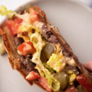 Taco on a plate with tomato, lettuce, cheese and pickles.