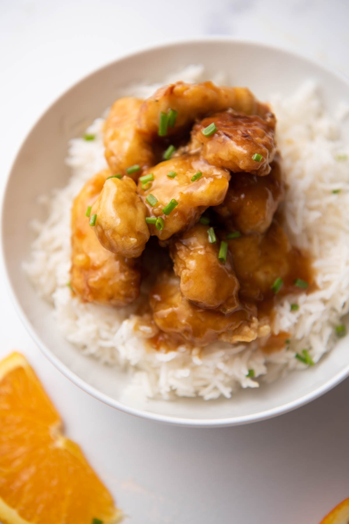 Orange chicken served over rice, garnished with chives.
