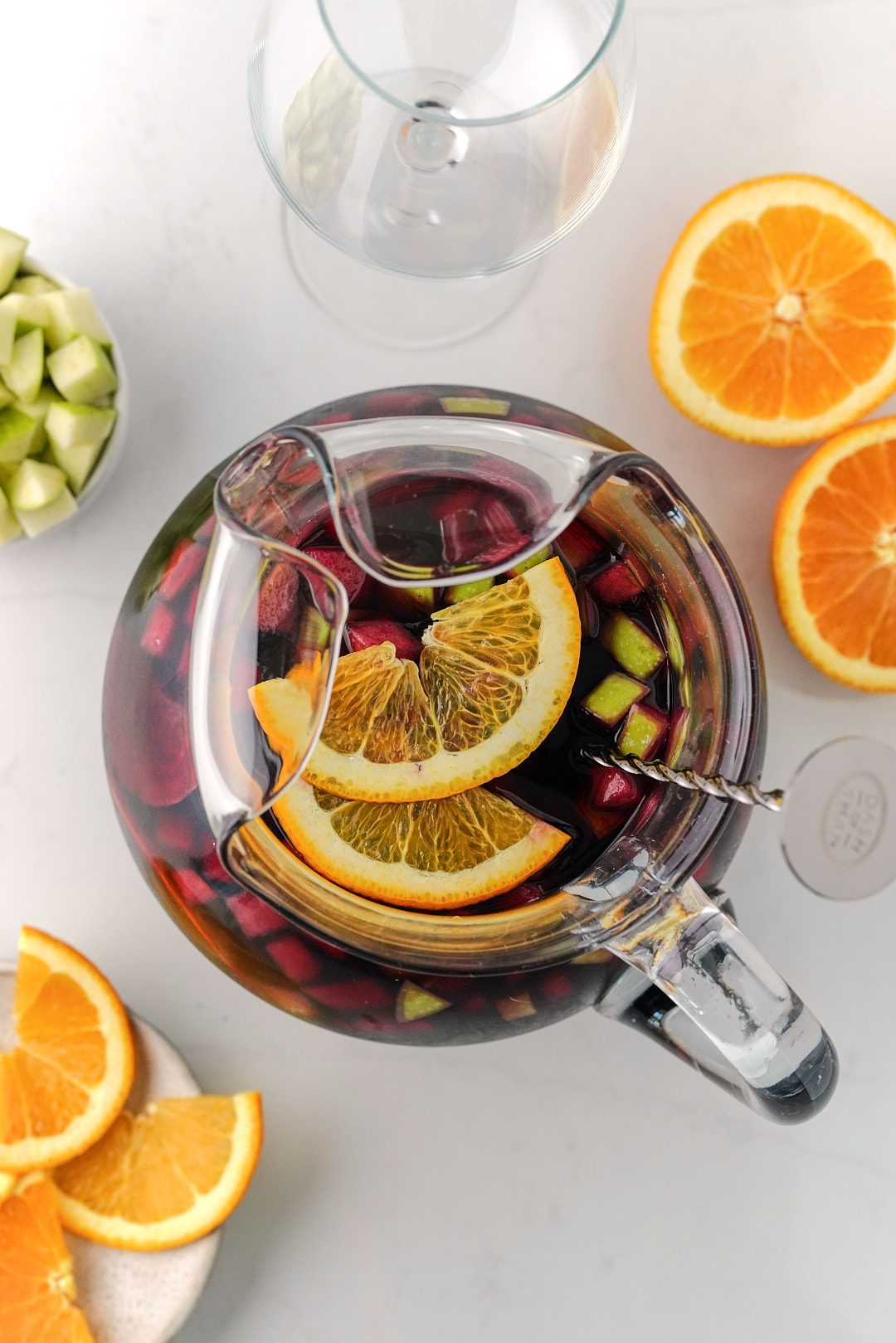 Overhead view of sangria in a glass pitcher with orange slices and long spoon.